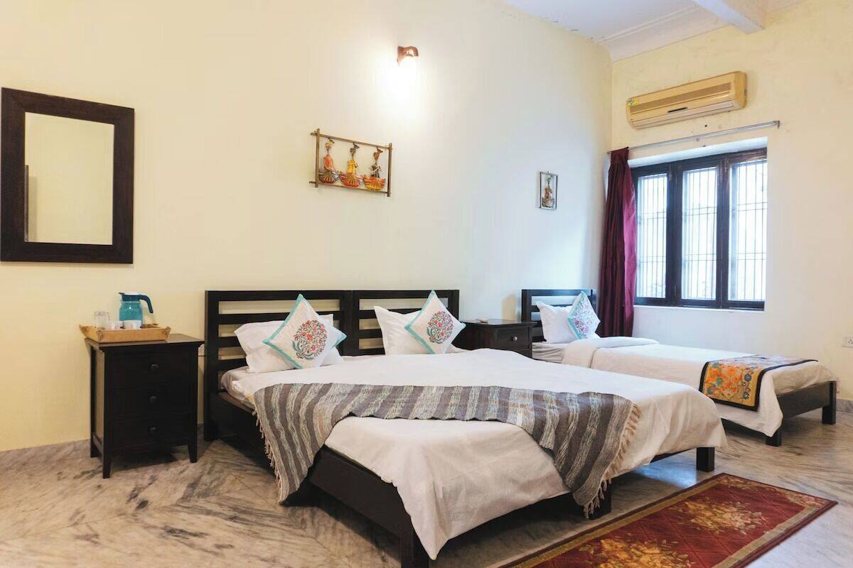 A hotel room with two beds, a nightstand, a mirror, an air conditioning unit, and a window with curtains.