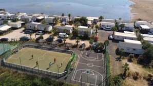 Un camping con vehículos recreativos, una cancha de baloncesto y una playa al fondo.
