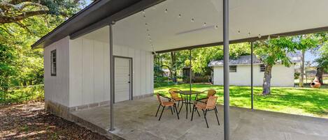 A covered patio with a concrete floor, a table with chairs, and a view of a house and trees.