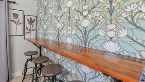 Eine Bar mit einer Holztresen und drei Hockern. An der Wand befindet sich ein floraler Wandbelag.