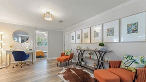Ein modernes Wohnzimmer mit Holzboden, einem Kuhfellteppich, einem blauen Bürostuhl, einem orangefarbenen Sofa und gerahmten Kunstwerken an der Wand.