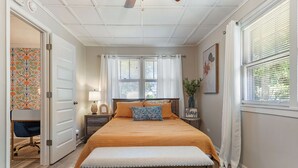 Ein Schlafzimmer mit Bett, Sitzbank, Nachttisch, Lampe und einer Tür zu einem weiteren Raum.