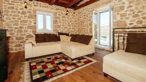 A cozy room with a stone wall, wooden ceiling beams, a white sofa, and a colorful rug. - Holiday Home Zaton with Pool near River Canyon (Obrovac)