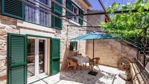 A stone building with green shutters, a table with chairs, and a wheelbarrow. - Holiday Home Zaton with Pool near River Canyon (Obrovac)