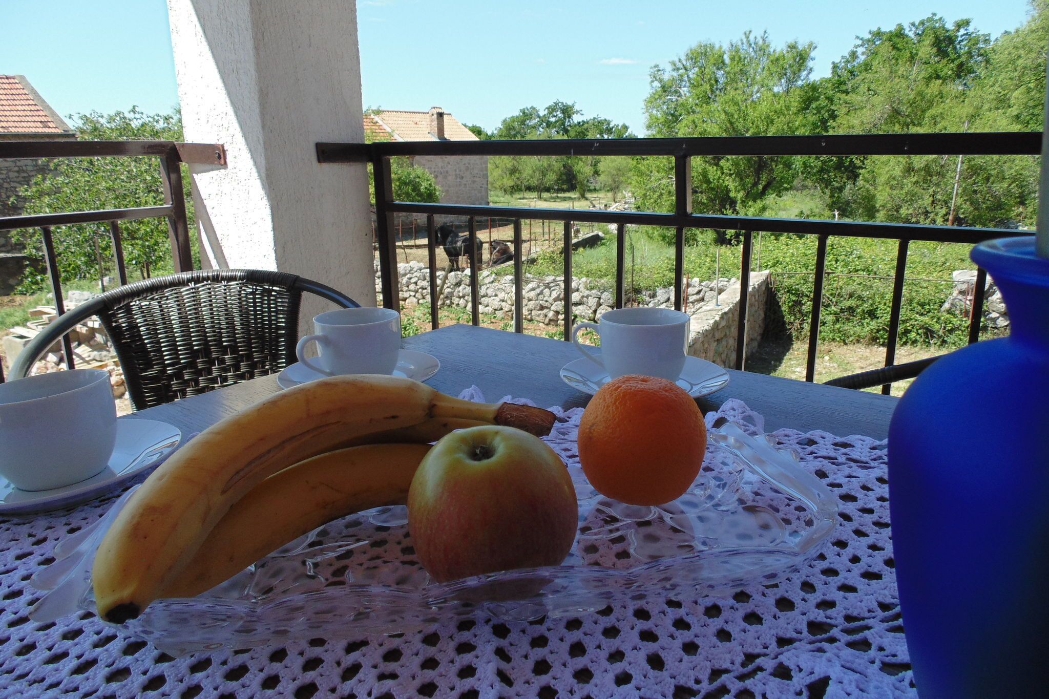 Une table recouverte d’une nappe en dentelle, avec une banane, une pomme et une orange.