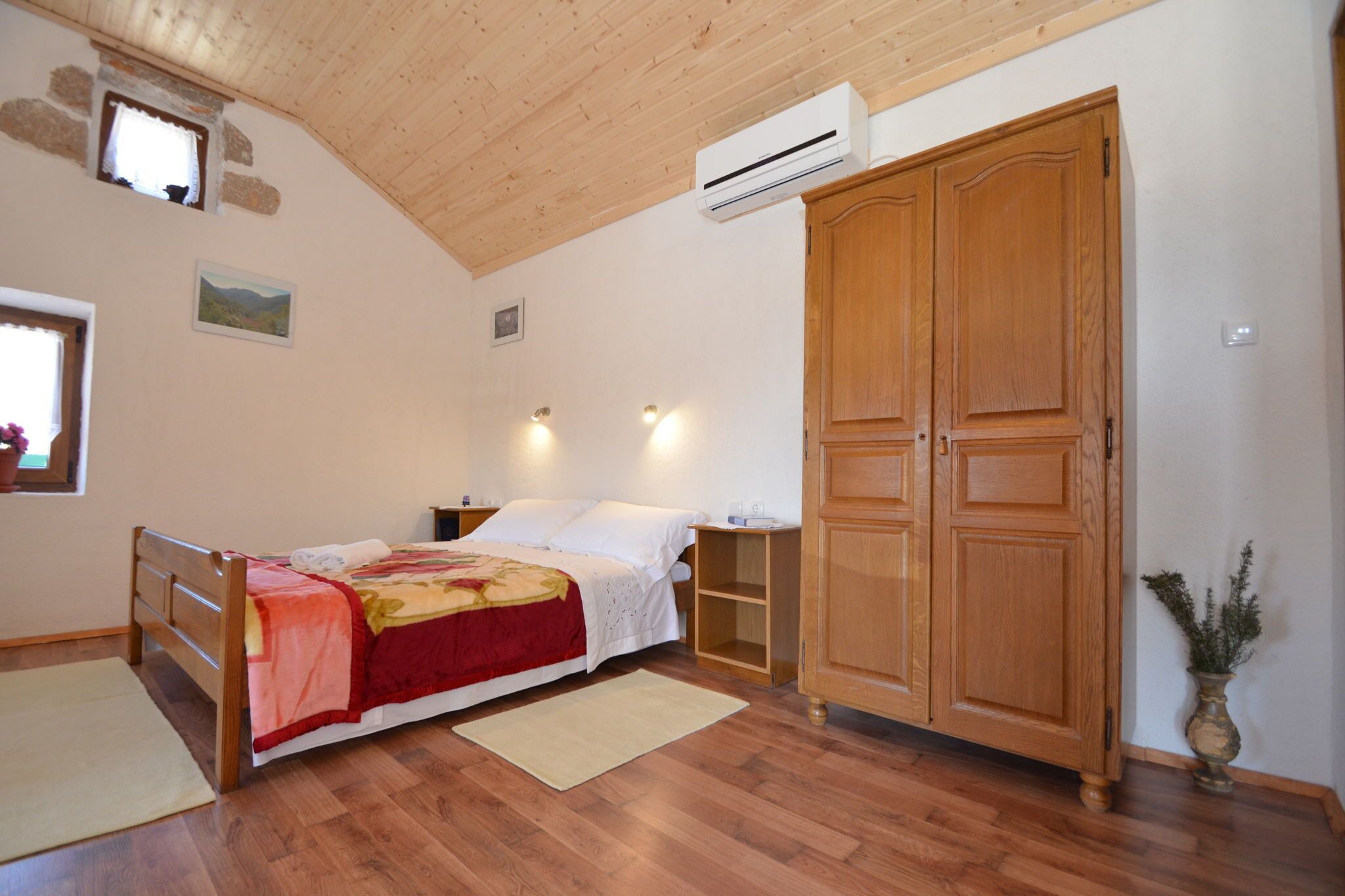 A bedroom with a wooden bed, a wardrobe, a window, and an air conditioning unit.