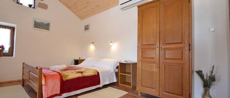 A bedroom with a wooden bed, a wardrobe, a window, and an air conditioning unit.