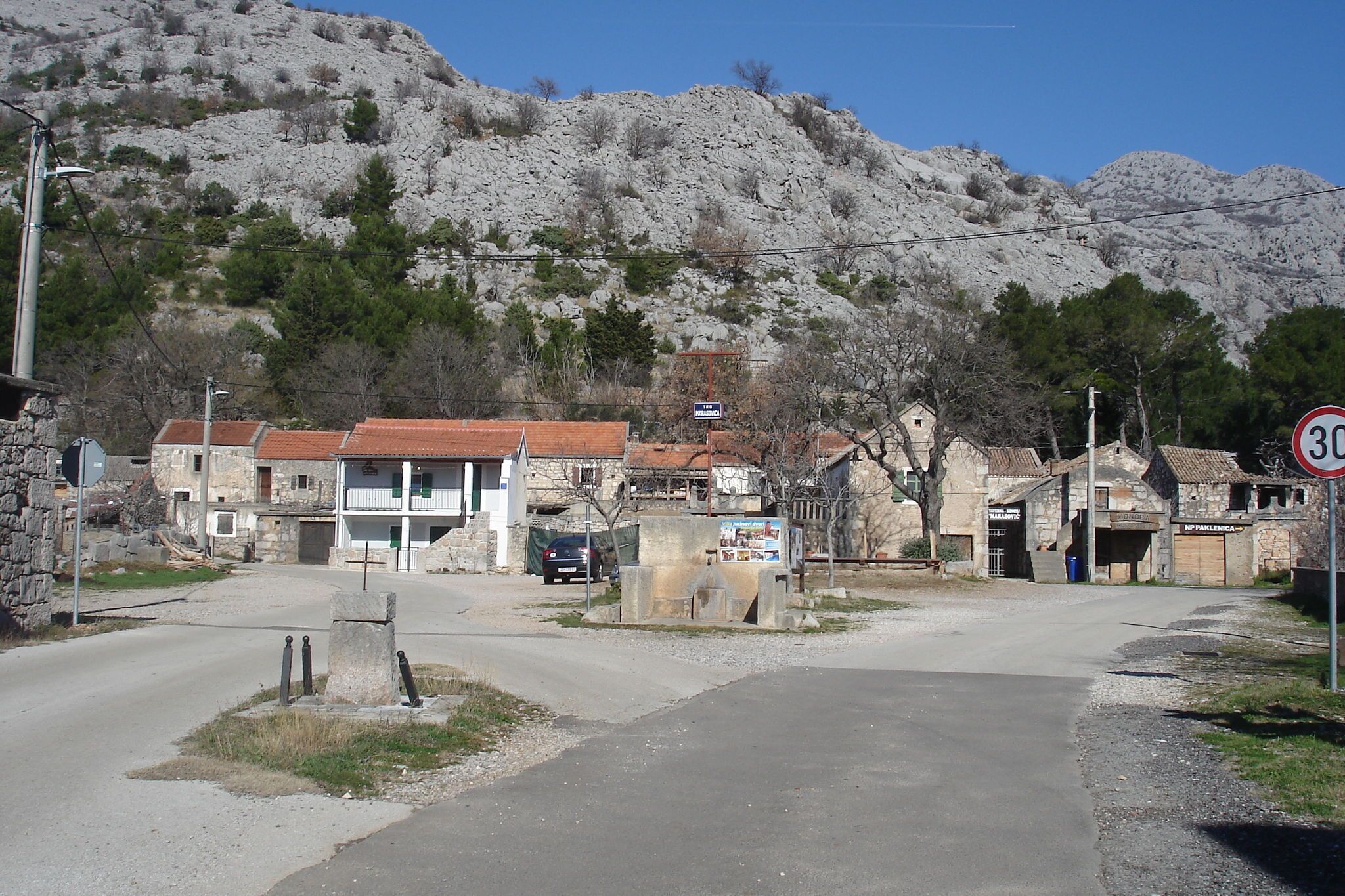 A rural village with stone buildings, a clear road, and a speed limit sign.