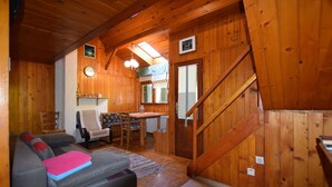 A cozy wooden cabin interior with a sofa, a dining table, and a staircase.