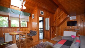 A wooden cabin interior with a dining area, sofa, and a TV mounted on the wall.