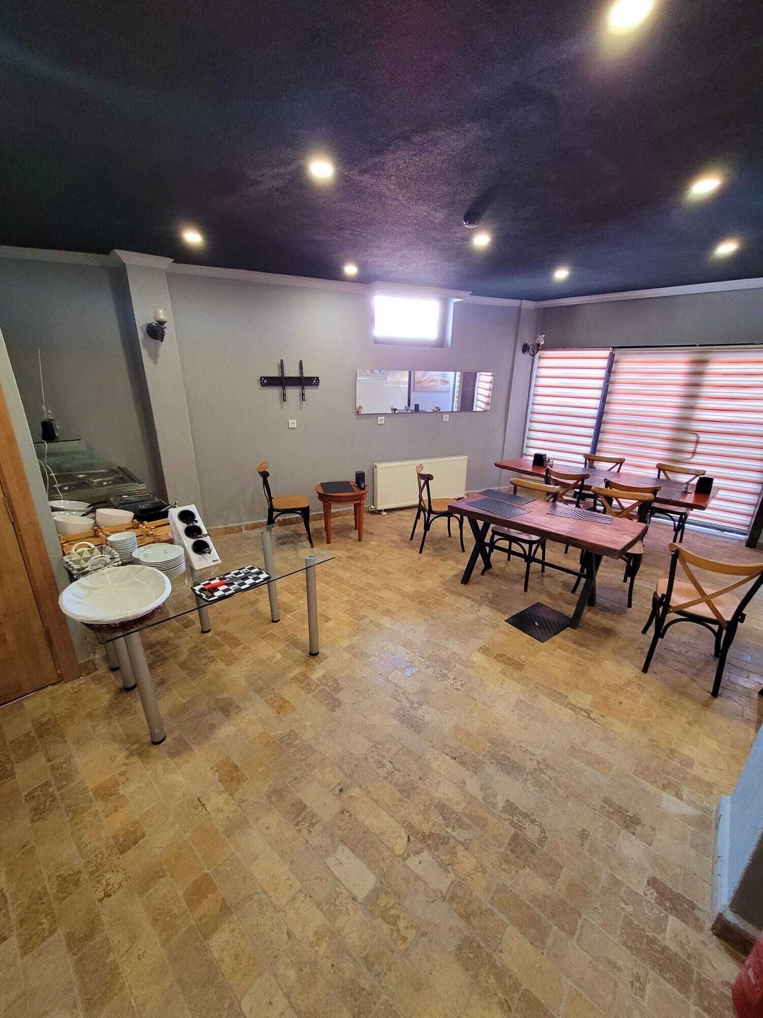 A spacious room with a large table and chairs, a small kitchen area, and a window with blinds.