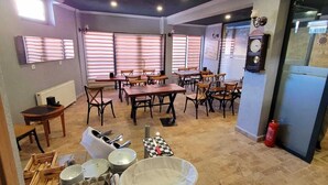 Un espace repas avec plusieurs tables et chaises, une vitrine où sont exposées des assiettes, et une horloge au mur.