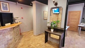 Un espace d’accueil comprenant un comptoir, un téléviseur fixé au mur, une plante en pot et un sol à motifs.