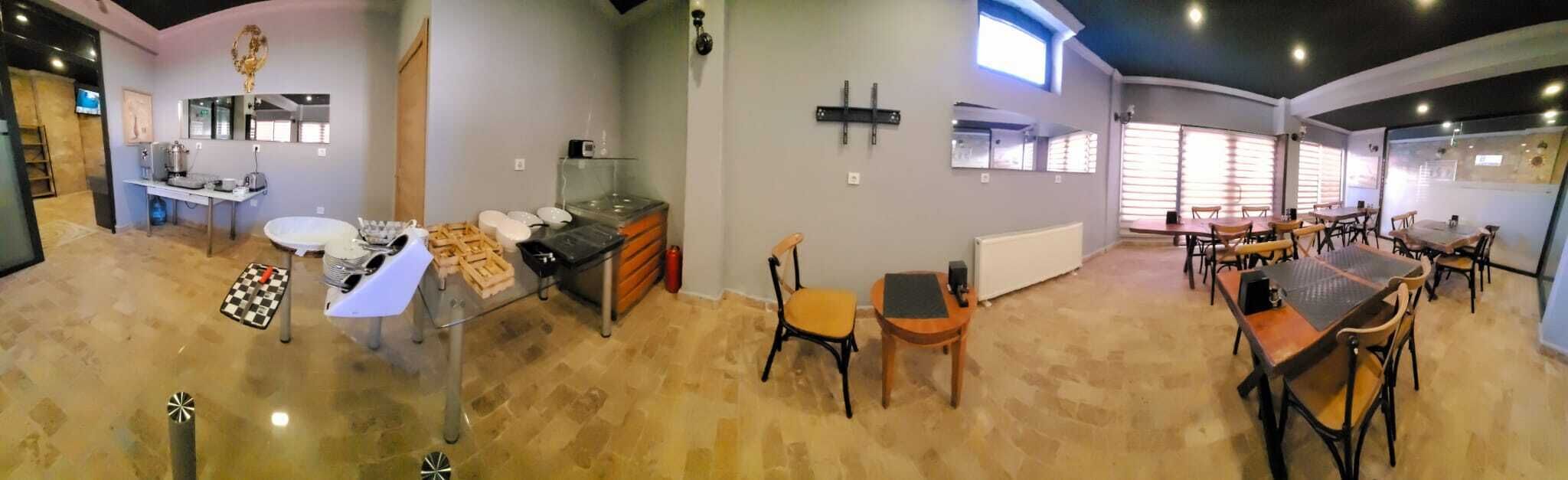 A spacious dining area with multiple tables and chairs, a kitchen area with a sink and stove, and a large window providing natural light.