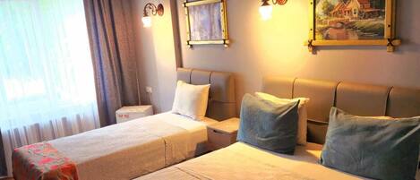 Habitación de hotel con dos camas, un ventanal con cortinas, un cuadro en la pared y una lámpara en el techo.