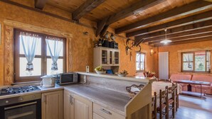 A rustic kitchen with wooden cabinets, a gas stove, a microwave, and a sink. There is a dining area with a wooden table and chairs. - Holiday Home in Gorski Kotar with Pool (Brod Moravice)