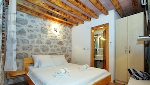A bedroom with a stone wall, wooden ceiling beams, a bed with white linens, a bedside table, and a wardrobe. - Holiday Home in Starigrad with Sea View (Starigrad - Paklenica)