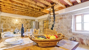 A rustic kitchen with exposed wooden beams, a stone wall, and a wooden table set for dining. - Holiday Home in Starigrad with Sea View (Starigrad - Paklenica)