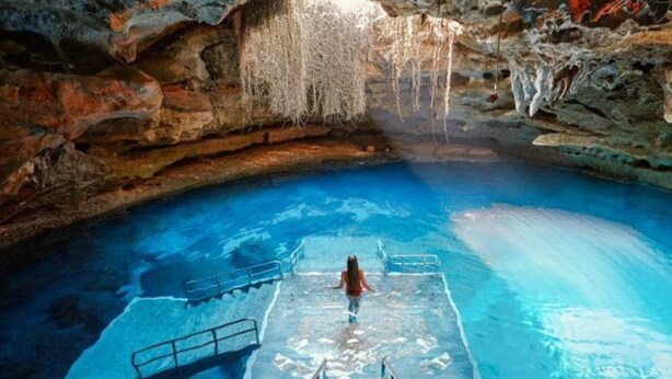 A pool with a wooden deck and a metal railing, surrounded by rocky cave walls. - Cozy Home In Beverly Hills near Crystal River, Florida (Beverly Hills)