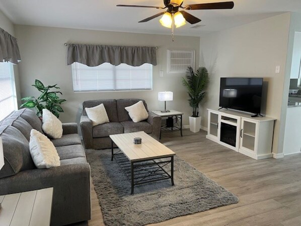 A living room with a sofa, coffee table, TV, and a ceiling fan.