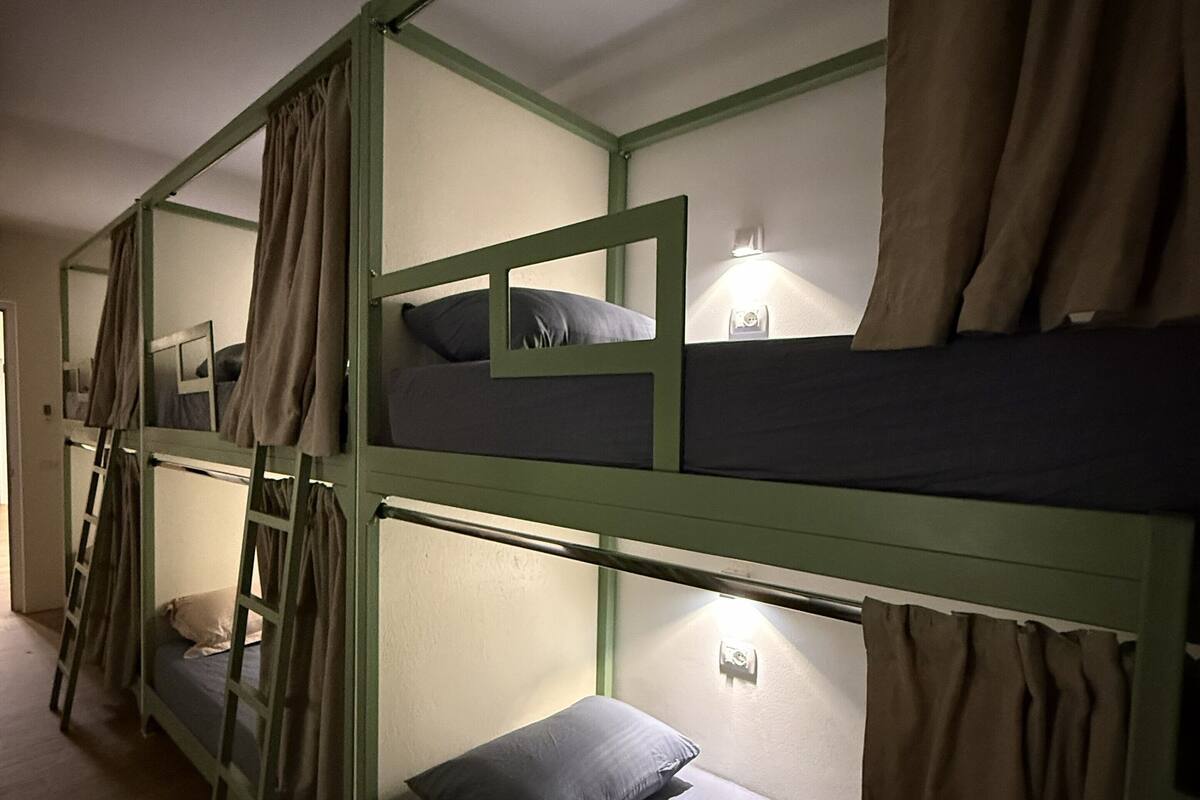 Une chambre avec un lit superposé, une échelle, une table de chevet avec une lampe et un luminaire fixé au mur.
