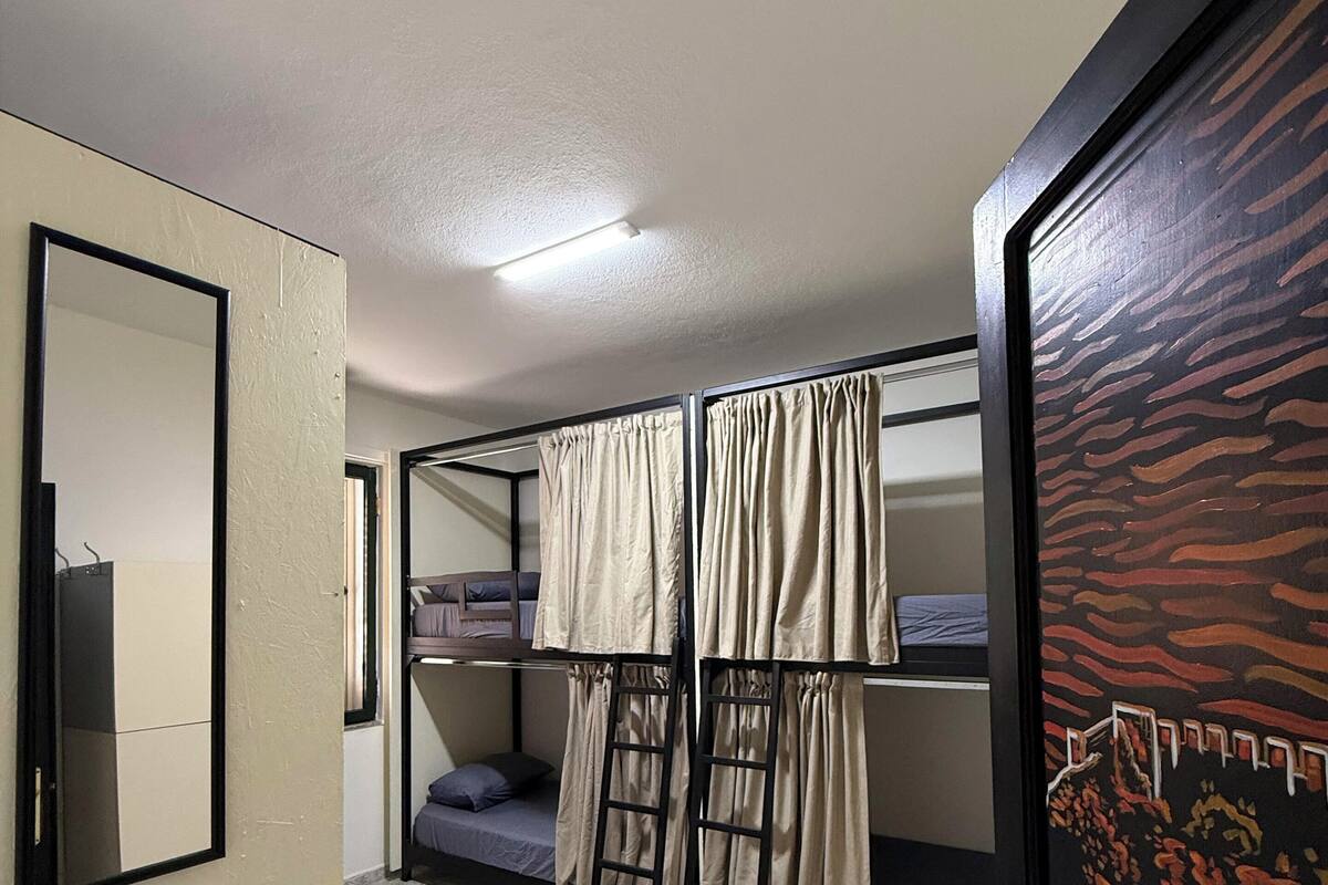 Une chambre de dortoir avec des lits superposés, une échelle, un miroir et une porte ornée d’un panneau décoratif.