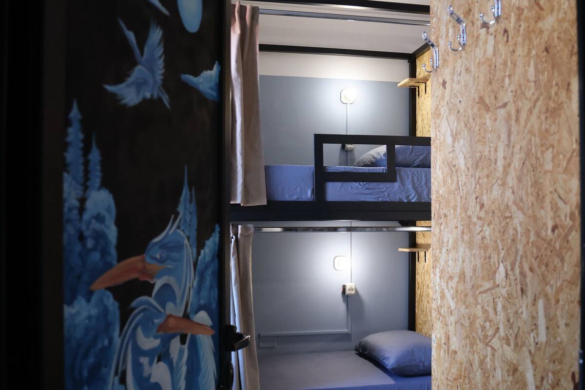 Une chambre de dortoir avec des lits superposés, un mur en bois et une porte ornée d’une fresque bleue et blanche.
