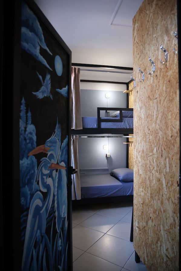 A dormitory room with bunk beds, a wooden wall, and a door with a blue and white mural. - Shkodra Hostel (Shkodër)