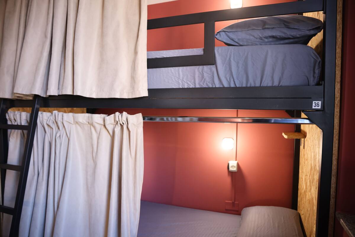 Un lit superposé avec un rideau, une table de chevet avec une lampe et un luminaire fixé au mur.