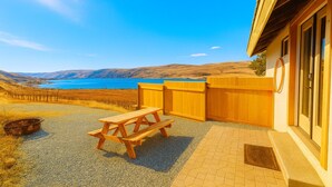 A wooden picnic table and bench in a backyard with a view of a lake and hills.