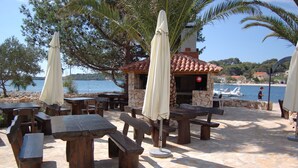 Un área de comedor al aire libre con mesas y bancos de piedra, sombrillas y vistas al mar.