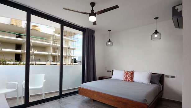 Ein modernes Schlafzimmer mit einem großen Bett, einem Deckenventilator und Blick auf ein im Bau befindliches Gebäude.