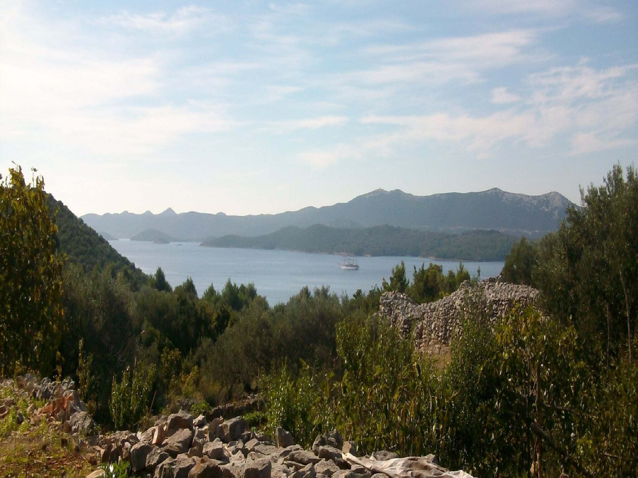 A coastal landscape with a rocky foreground, a body of water, and distant mountains.
