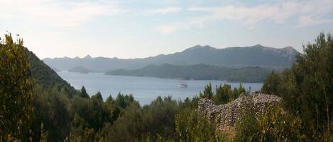 A coastal landscape with a rocky foreground, a body of water, and distant mountains.