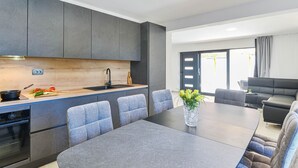 A modern kitchen with grey cabinets, a wooden countertop, and a black faucet. There is a dining table with grey upholstered chairs and a vase of yellow flowers. - Holiday Home Bibinje near the Sea (Bibinje)