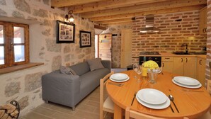 A cozy room with a grey sofa, wooden dining table set for two, and a kitchen area with a brick wall and wooden ceiling. - Seaside Retreat in Marina di Grosseto (Starigrad Paklenica)