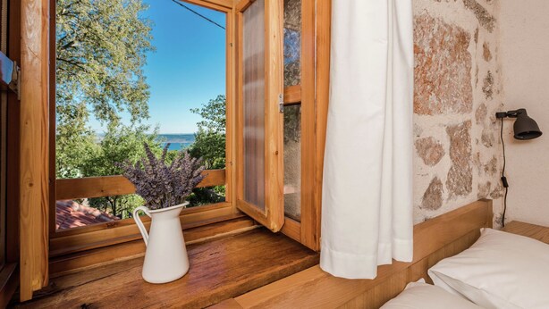 A wooden-framed window with a view of trees and a body of water. A white vase with purple flowers is on the windowsill. - Seaside Retreat in Marina di Grosseto (Starigrad Paklenica)