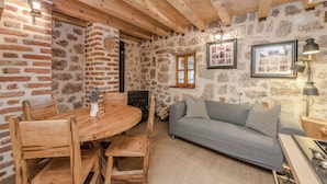 A rustic room with a stone wall, wooden ceiling beams, a round wooden table with chairs, a grey sofa with patterned cushions, and a framed picture on the wall. - Seaside Retreat in Marina di Grosseto (Starigrad Paklenica)
