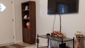 A living room with a dark wooden bookshelf, a flat-screen TV mounted on the wall, a small table with decorative items, and a patterned rug on the floor. - Cozy 2-bedroom bungalow with AC and WiFi in charming Springfield (Springfield)