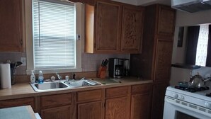 A kitchen with wooden cabinets, a sink, a stove, and a window with blinds. - Cozy 2-bedroom bungalow with AC and WiFi in charming Springfield (Springfield)