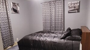 A bedroom with a bed, patterned curtains, and two framed pictures on the walls. - Cozy 2-bedroom bungalow with AC and WiFi in charming Springfield (Springfield)