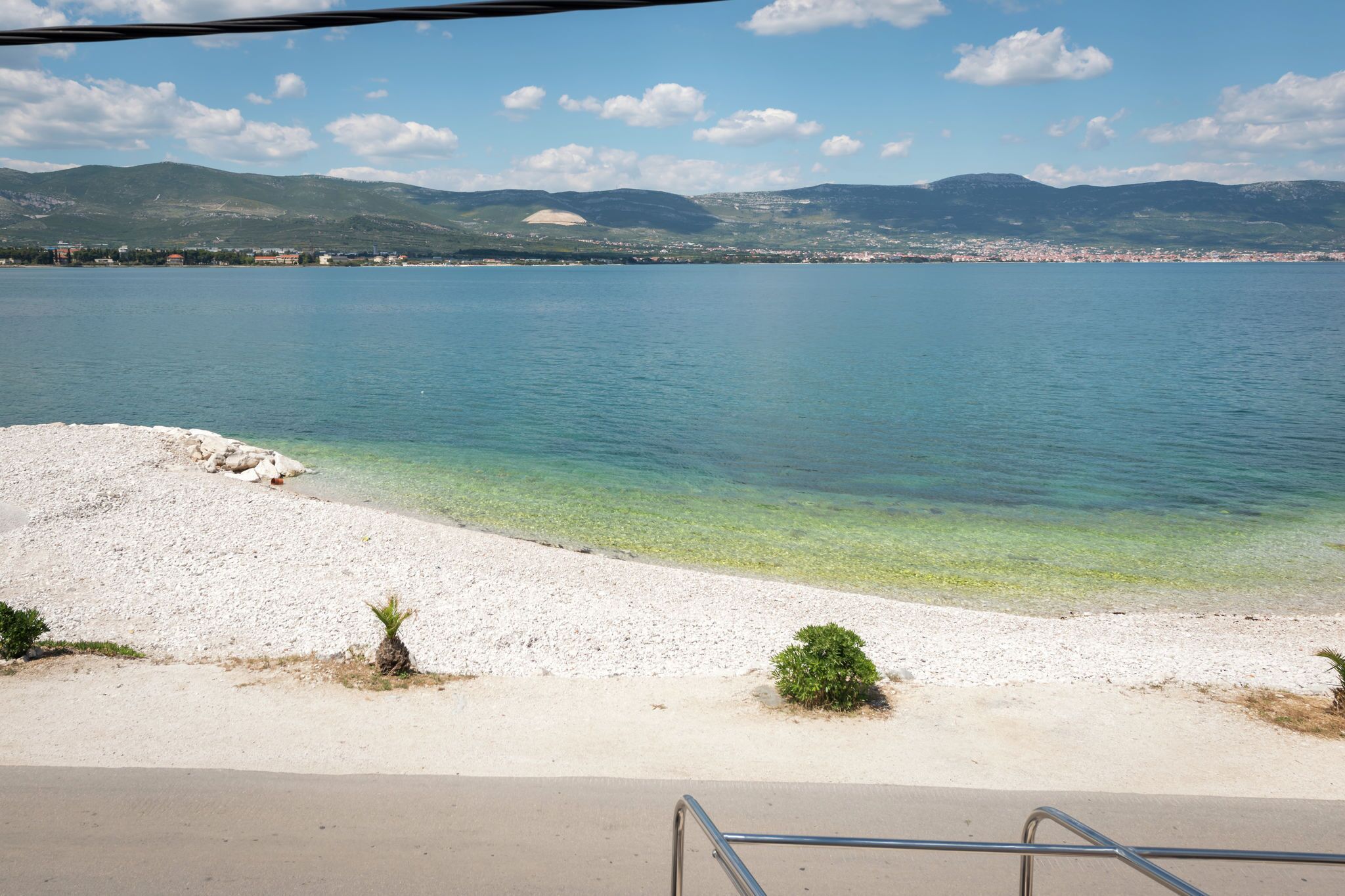 A beach with clear water, a sandy shore, and mountains in the background.