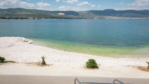 Une plage à l’eau claire, un rivage sablonneux et des montagnes en arrière-plan.