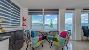 Une cuisine moderne avec vue sur la mer, deux chaises colorées et un coin repas agrémenté d’un parasol vert.