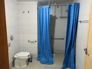 A small, compact bathroom with a toilet, a shower stall, and a handrail. - Saint Sebastian ap103-stúdio (Jaragua do Sul)