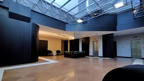 A spacious lobby with a high ceiling, a glass atrium, and a reception area with a desk and chairs. - Saint Sebastian ap103-stúdio  (Jaragua do Sul)