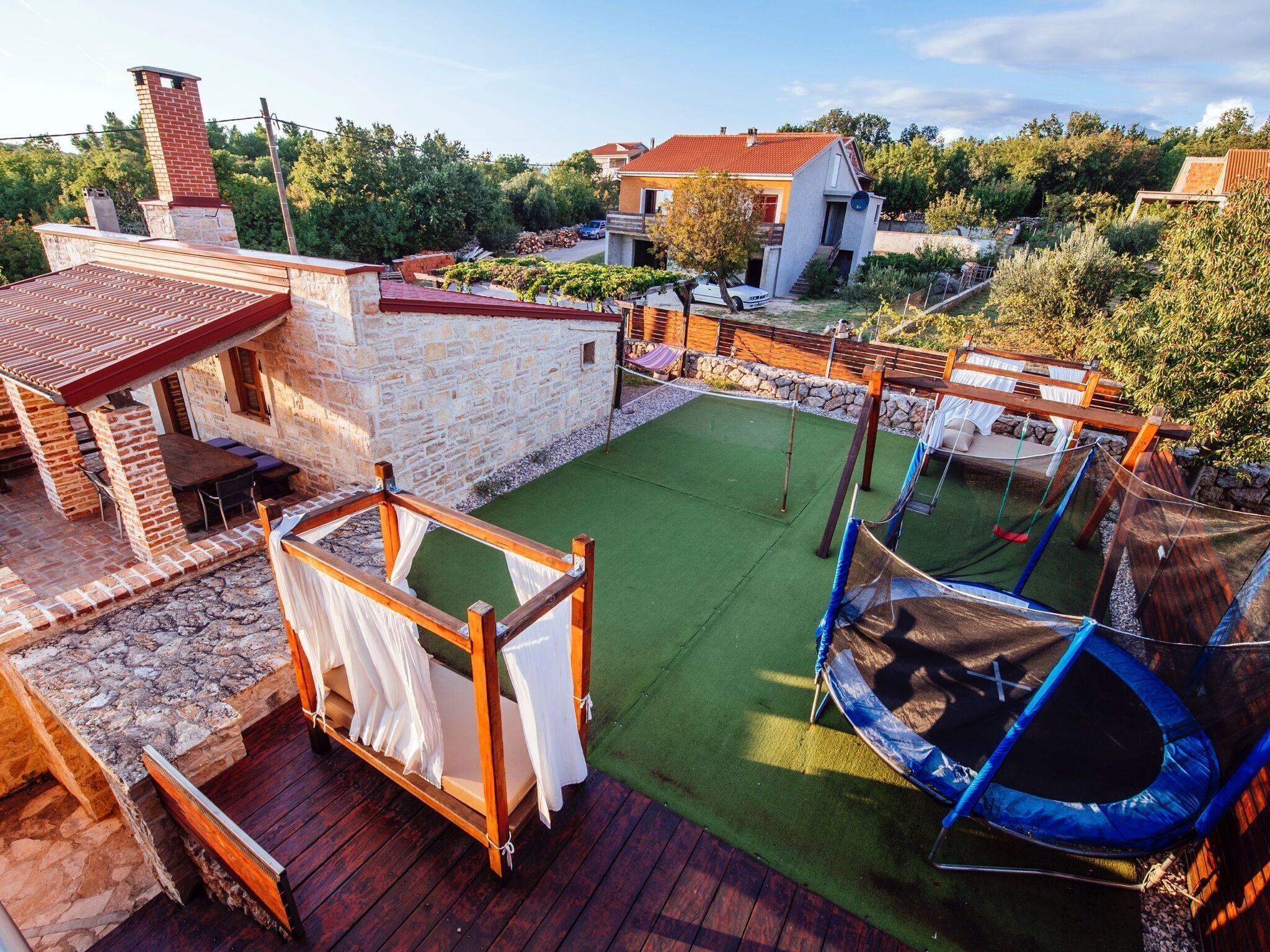 A backyard with a trampoline, a wooden deck, and a stone wall.