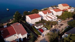 Vue aérienne d’un quartier résidentiel situé sur la côte, avec des maisons, un bateau sur l’eau et une vue dégagée sur la mer.