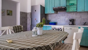 Une cuisine de taille réduite avec des meubles de couleur turquoise, un réfrigérateur et un coin repas agrémenté d’une nappe à carreaux.