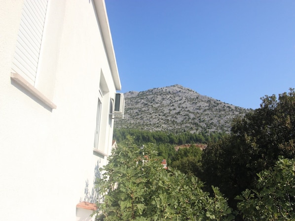 Un bâtiment à l’extérieur blanc, une fenêtre avec un appareil de climatisation et une montagne en arrière-plan.